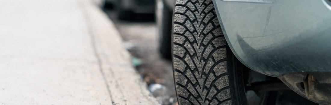 Close-up of a car parked on a hill, with the tire turned into the curb to stop  the car from rolling forward.