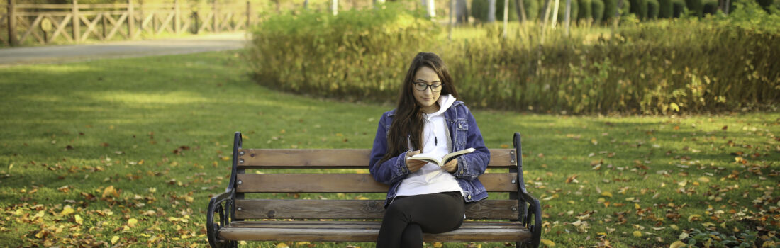 Girl sitting on the bench at the park and reading a book.