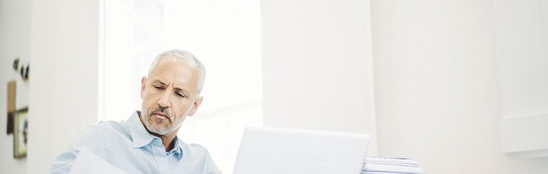 Businessman reading document at desk in office Businessman reading document at desk in office. Executive is with papers and laptop on table. Mature professional is working in brightly lit office.