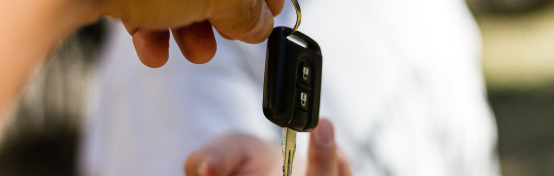 Young adult girl receives the key of her new car. Business transport trade concept. Car sales and rental assistance. Selective focus on the car key.