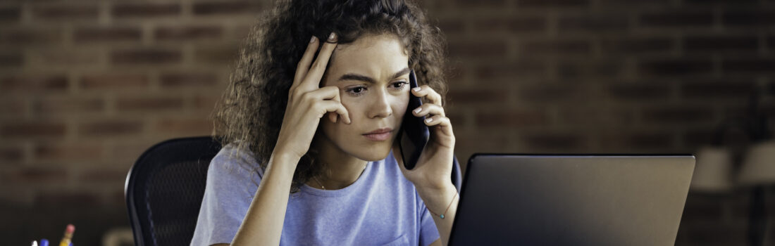 Working home: Hispanic curly hair worried young woman using laptop and working at home office. Low key scene captured in a rustic kitchen.